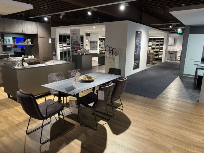 dunkle. gepolsterte Esszimmerstühle mit Kufengestell rund um einen eckigen Tisch in der Möbel Nachtsheim Ausstellung