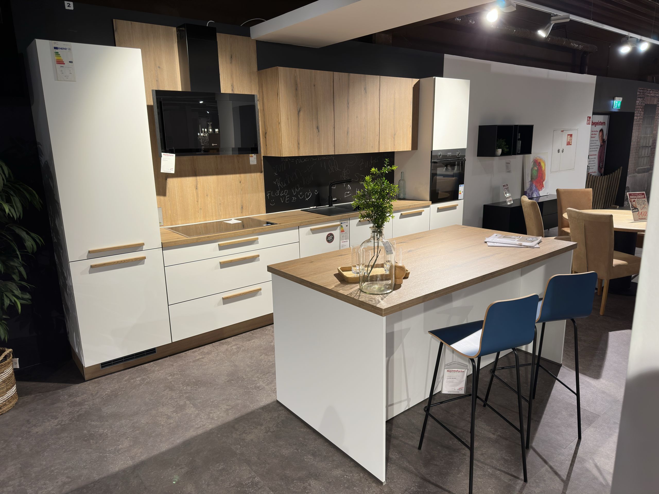 Wohnküche mit weißen und Holzoptik-Oberflächen, zwei Barhocker vor der Kücheninsel, die als Esstisch fungiert